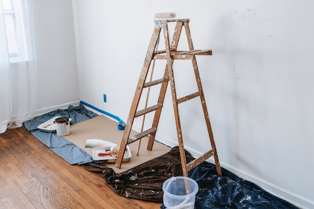 an open ladder on a black tarp for painting with paint next to it on the ground